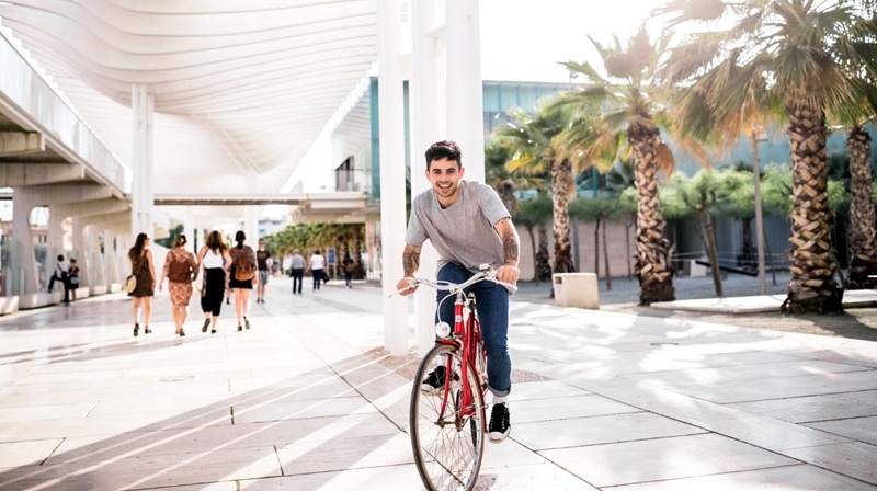 a man cycling in the street by palm trees